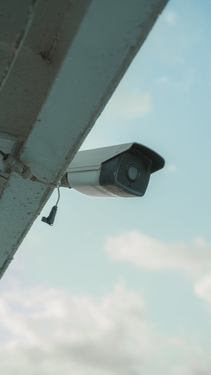 A security camera mounted on a building eaves under a clear blue sky.
